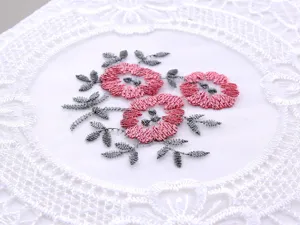 Dettaglio ravvicinato del ricamo a fiori rosa su tovaglia in filato di vetro bianco