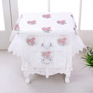 Dettaglio del coprimobile in pizzo bianco con delicati ricami floreali rosa su filato di vetro.