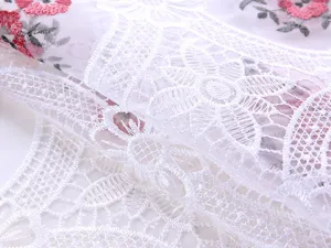 Dettaglio della tovaglia in filato di vetro bianco con ricamo floreale rosa e pizzo