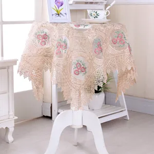 Elegante tovaglia in pizzo beige con ricami floreali rosa su un piccolo tavolo rotondo.