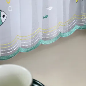 Detailed macro shot of white lace dust cover showing green fish embroidery and wavy edge
