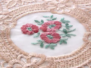 Vista dettagliata del ricamo floreale rosa su organza bianca e tovaglia in pizzo beige