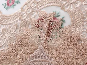 Dettaglio macro di elegante ricamo in pizzo champagne su tovaglia in filato di vetro