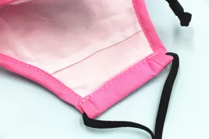 Detailaufnahme des weißen Innenfutters und der Nähte einer rosa Baumwoll-Gesichtsmaske