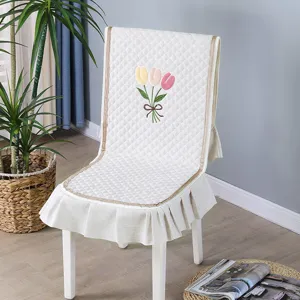 White quilted chair cover with tulip embroidery and ruffled edge for dining chairs.