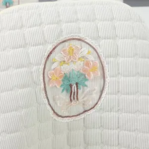 Close-up detail of white quilted chair cover featuring colorful floral embroidery patch