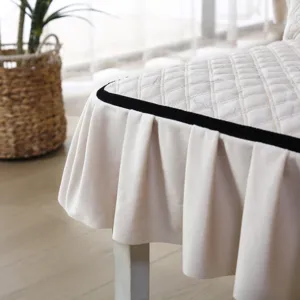 Close-up detail of beige quilted chair cover with pleated skirt and black ribbon trim.