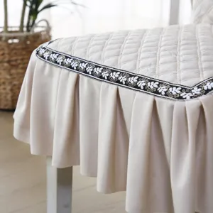 Détail d'une housse de chaise matelassée beige avec bordure brodée et jupe à volants.