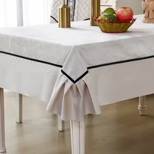 Detailed view of elegant cream tablecloth featuring black trim and decorative pleated corners