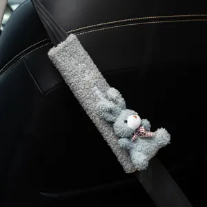 Detailed close-up of a cute gray plush rabbit car seat belt cover on a black leather seat