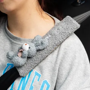 Detalle de funda de cinturón de seguridad de felpa gris con bordado de oso y conejo.