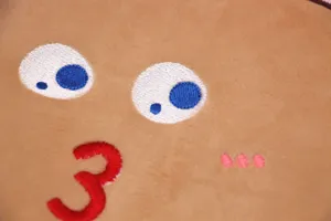 Dettaglio ricamo custodia iPad a forma di toast in morbido peluche con faccia buffa.
