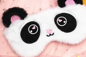 Close-up detail of a soft plush panda sleep mask featuring cute pink heart embroidery
