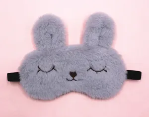 Macro view of a cute grey plush bunny sleep mask with embroidered eyes on pink background