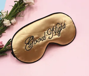 Nahaufnahme goldene Schlafmaske mit Good Night Stickerei auf rosa Hintergrund