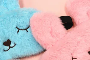 Detailed close-up of soft plush rabbit sleep masks in pink and blue with cute embroidery.