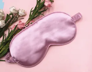 Close-up detail of a soft pink silk sleep mask featuring smooth satin texture and elastic strap