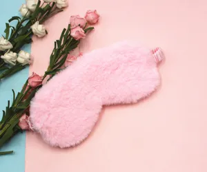 Close-up macro view of soft plush pink rabbit fur eye mask on cozy floral background