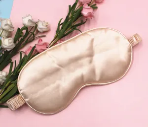 Close-up of champagne silk sleep mask with elastic strap on pink floral background