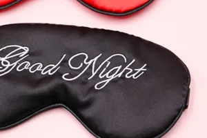 Nahaufnahme der schwarzen Satin-Schlafmaske mit weißer Good Night Stickerei-Detail.