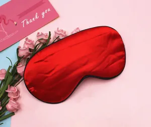 Detailed shot of a luxury red satin sleep mask on a pink background with roses