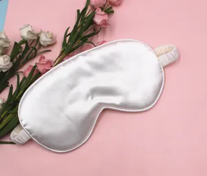 Detailed view of a soft white satin sleep mask placed on a pink floral background.