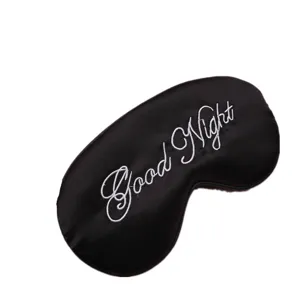 Nahaufnahme der weißen 'Good Night' Stickerei auf einer schwarzen Seiden-Schlafmaske aus Satin