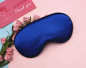 Close-up of silky blue sleep eye mask with soft blackout fabric on pink background