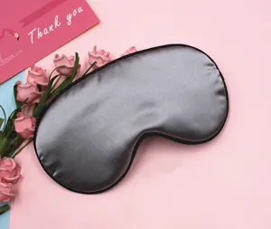 Detailed view of soft silver satin sleep mask with elegant black piping on pink background.