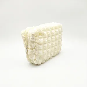 Detailed view of the bubble textured fabric and sturdy zipper on this white cosmetic pouch.
