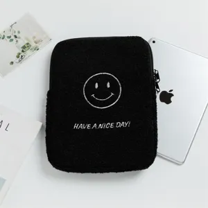 Custodia per iPad in peluche nera con ricamo a faccina sorridente vicino al tablet.