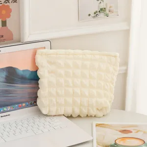 Primer plano de un neceser crema con textura de burbujas sobre un escritorio blanco.