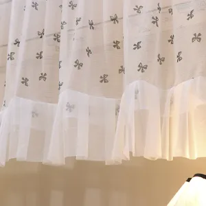 Detailed close-up of white lace sheer curtain featuring elegant bow patterns and ruffled hem