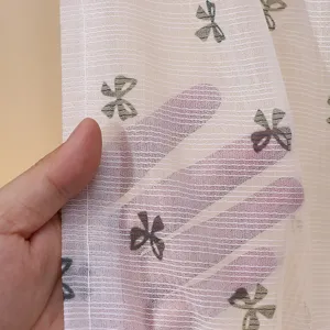 Detailed macro shot of semi-transparent lace curtain fabric with embroidered bow motifs.
