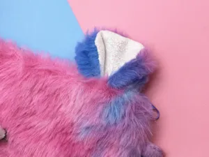 Macro detail showing soft pink and blue faux fur texture with a white glittery ear