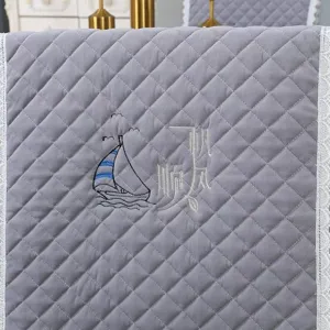 Close-up view of a gray quilted chair cover featuring sailboat embroidery and lace