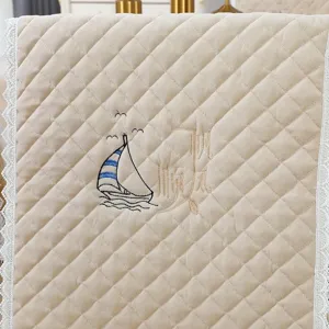 Close-up of beige quilted chair cover with sailboat embroidery and white lace trim