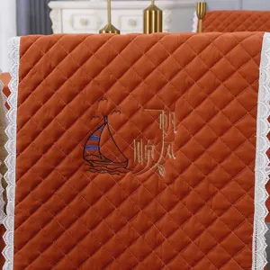 Close-up of orange quilted chair back cover with sailboat embroidery and lace edge.