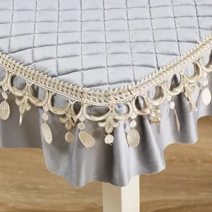 Dettaglio della tovaglia grigia trapuntata con bordo in pizzo dorato e pendenti eleganti