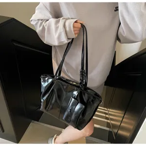 Detail einer glänzenden schwarzen Ledertasche, die von einem Model getragen wird