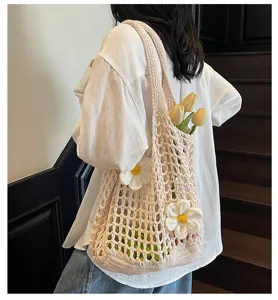Detalle de un bolso tote de malla tejida crema con detalles florales 3D al hombro.