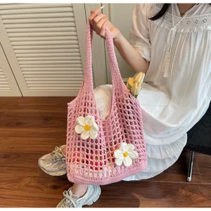 Detalle de un bolso tote de malla de ganchillo rosa con flores tejidas blancas y una modelo.