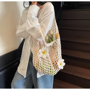 Detalle de un bolso de malla de ganchillo crema con flores en 3D llevado al hombro.