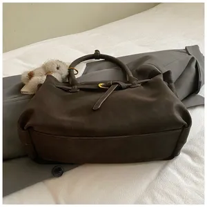 Close-up of large brown matte suede tote bag with belt buckle detail on a bed.