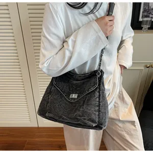Sac à bandoulière en denim noir délavé avec chaîne en métal, porté par un mannequin chic.