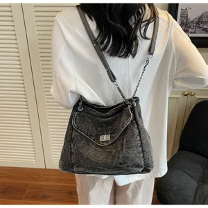 Détail d'un sac à bandoulière en denim noir délavé avec fermoir argenté et chaîne