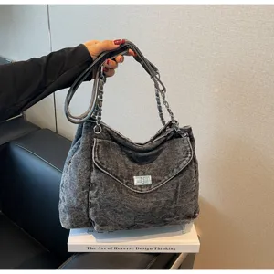 Détail d'un sac cabas en denim délavé avec bandoulière chaîne et fermoir métallique