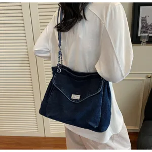 Détail d'un sac bandoulière en denim bleu foncé avec fermoir argenté porté par mannequin