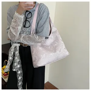 Détail d'un sac cabas rose brodé avec des motifs de papillons porté par un mannequin