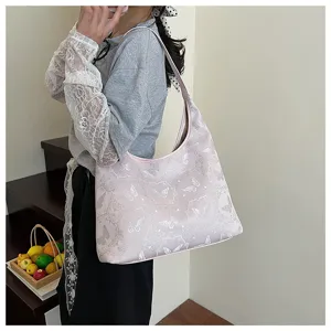 Sac cabas rose élégamment brodé de motifs de papillons porté par un mannequin à l'épaule.